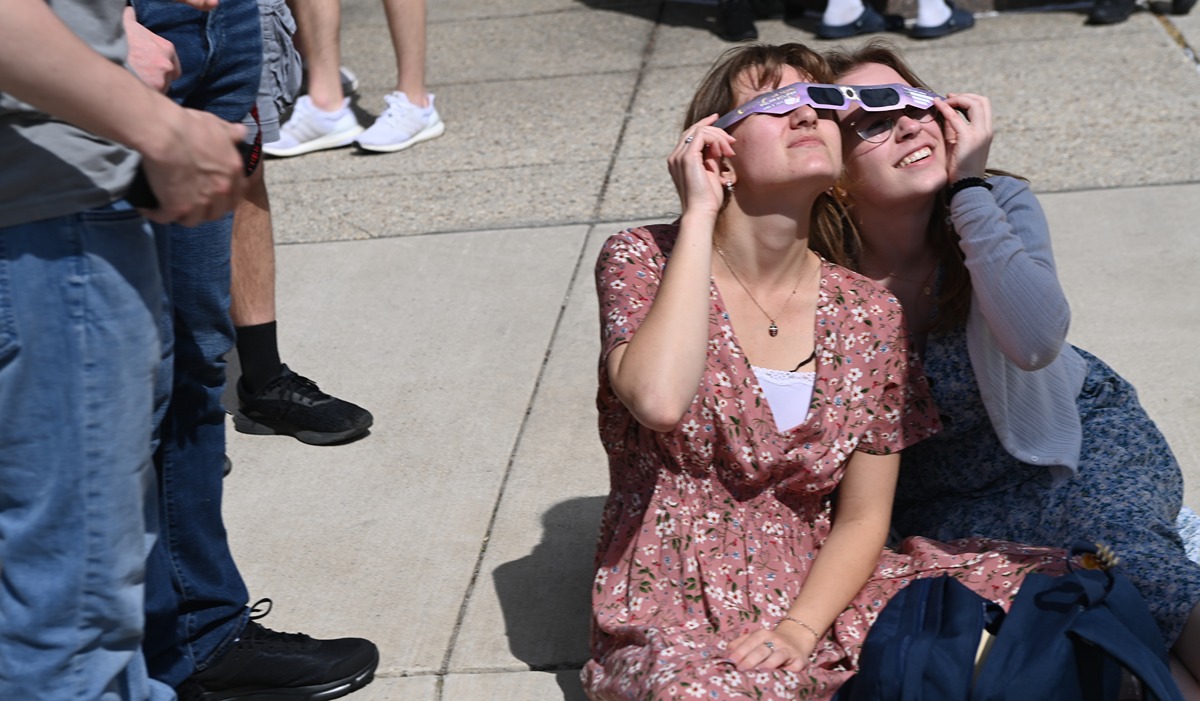students watch the eclipse through their protective glasses on campus