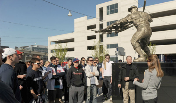 A Catholic ҽ class standing next to a baseball statue on a class outing.